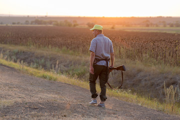 Wall Mural - Hunting period, autumn season open. A hunter with a gun in his hands in hunting clothes in the autumn forest in search of a trophy. A man stands with weapons and hunting dogs tracking down the game.	