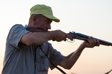 Wall Mural - Hunting period, autumn season open. A hunter with a gun in his hands in hunting clothes in the autumn forest in search of a trophy. A man stands with weapons and hunting dogs tracking down the game.	