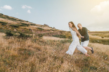 Young couple man and woman in love walking on the field on the mountain in autumn or summer day hugging together having fun bonding flirting flirt husband and wife lovers