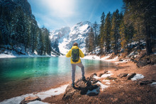 Sporty Man With Backpack Is Standing  On The Stone Near Lake With Azure Water At Sunny Day In Autumn. Travel. Landscape With Guy, Reflection In Water, Snowy Mountains, Orange Trees, Blue Sky In Fall