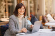 © igishevamaria - Young woman in warm sweater and blazer working on net-book in cafe on the terrace.  Autumn morning. Street style.