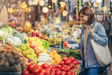 Woman is chooses fruits and vegetables at food market. Reusable eco bag for shopping. Sustainable lifestyle. Eco friendly concept.