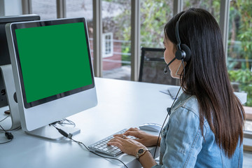 Call center woman sitting in customer service office in front of the computer, green screen with clipping path