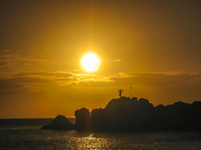 Sun Setting Behind Silhouette  Of Cliff Diver Performing Daily Tiki Torch Lighting Ceremony At Black Rock In Maui, Hawaii 