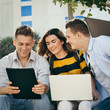 © nuiiko - Happy university student using laptop together outside building with natural light.