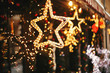 © sonyachny - Stylish christmas golden star illumination and fir branches with red and gold baubles, golden lights bokeh on front of building at holiday market in city street. Christmas street decor