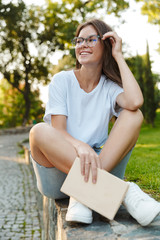 Sticker - Smiling young girl holding a book while sitting in the park