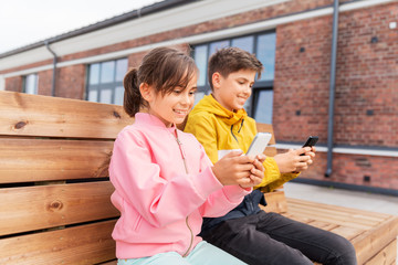 Sticker - childhood, technology and people concept - happy children or brother and sister with smartphones sitting on wooden street bench outdoors