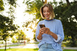 © Drobot Dean - Image of smiling woman typing on cellphone while resting in park