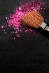 Wall Mural - Make-up brush with vibrant crushed cosmetics, shot from the top on a black background with copy space, a beauty design template for a makeup banner