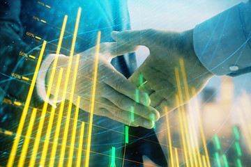 Double exposure of financial graph on cityscape background with two businessman handshake. Concept of stock market deal