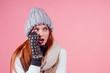 © yurakrasil - amazed redhaired ginger woman wearing stylish hat ,knitted mittens and sweater gossiping in studio pink background