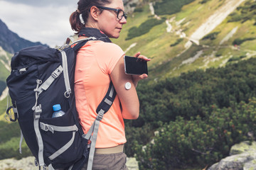 Wall Mural - Active life of diabetics, woman hiking and checking glucose level with a remote sensor and mobile phone, sensor checkup glucose levels without blood