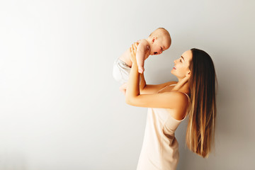 Wall Mural - Beautiful mother holds her baby on a plain light background.