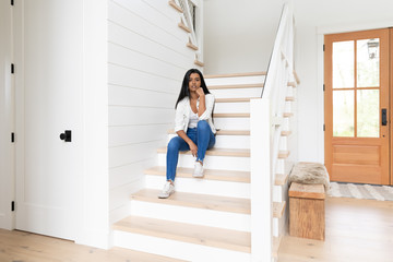 Indian woman sitting on the stairs of her modern brightly lit suburban home