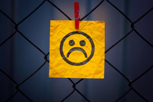 Yellow Paper Note With Sad Face Hanging On A Metal Mesh Fence