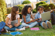 © InsideCreativeHouse - Happy little school children with digital gadgets and backpacks sitting at the grass park outdoors