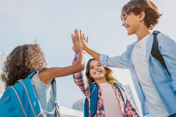 Happy children giving high five each other standing near school outdoors