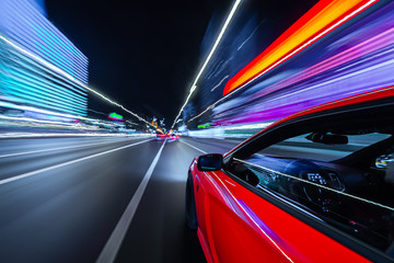 Wall Mural - View from Side of a Red Muscle Car moving in a night city, Blured road with lights with car on high speed. Concept rapid rhythm of a modern city.