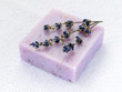 Handmade soap bar with dry aromatic lavender flowers. Purple  soap on a white terry cotton towel. Natural toiletries and hygiene products with herbs and essential oils.
