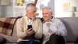© motortion - Elderly males holding smartphone sitting home sofa, online internet connection