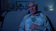 © motortion - Elderly man holding remote controller sleeping in front of TV, evening at home