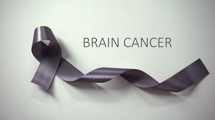 Wall Mural - Brain cancer inscription, gray ribbon lying on table, awareness campaign, ad