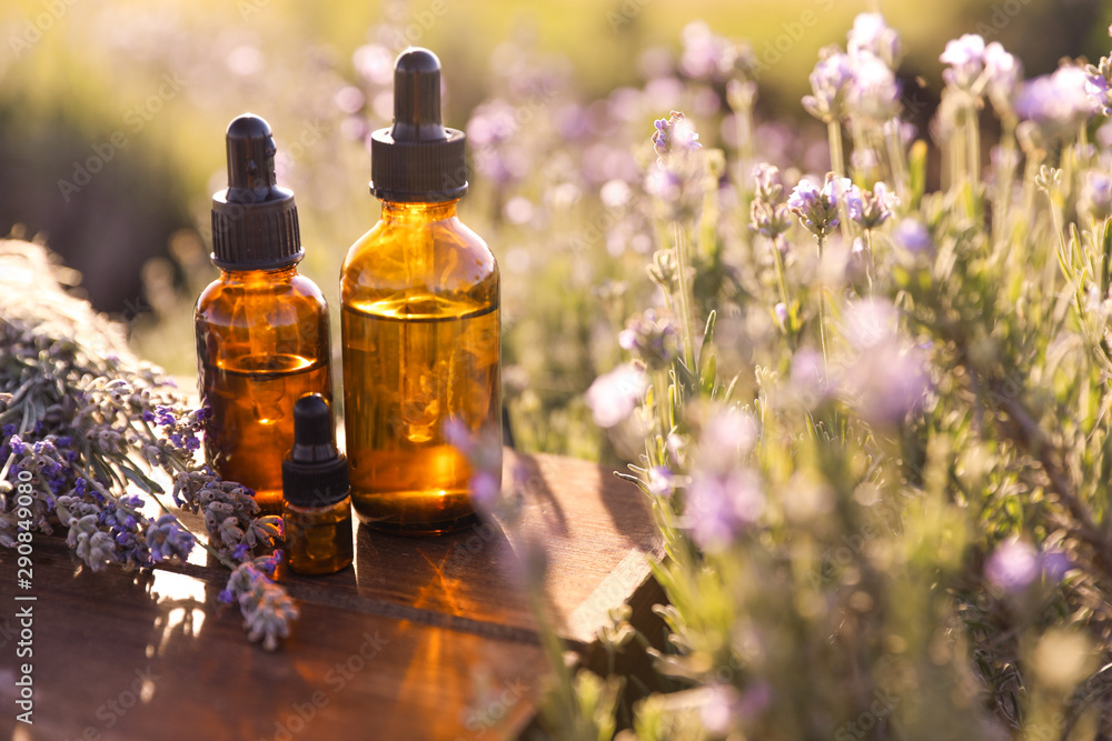 Bottles of lavender essential oil on wooden table in field. Space for text - obrazy, fototapety, plakaty 