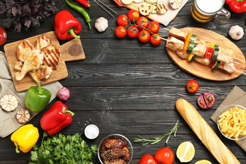 Frame of barbecued meat and vegetables on black wooden table, flat lay. Space for text