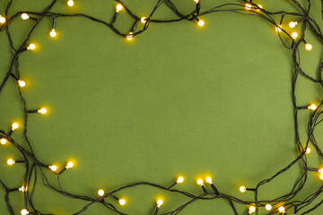 Wall Mural - Frame made with Christmas lights on green background, top view. Space for text