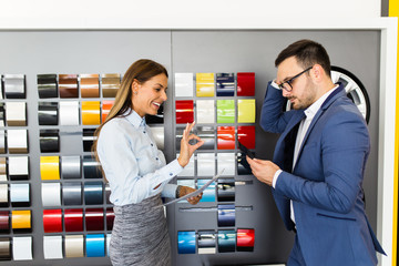 Wall Mural - Young handsome man talking with saleswoman and choosing a color for his new car at car showroom.