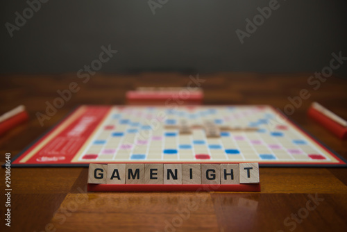 Letter tiles spelling out the words game night on stand in the foreground with out of focus game board in the background.