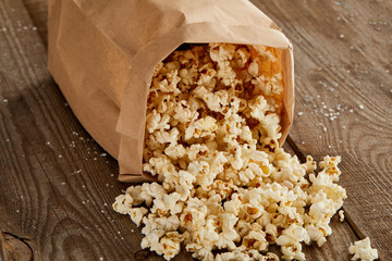 Sticker - delicious popcorn scattered from paper bag on wooden background