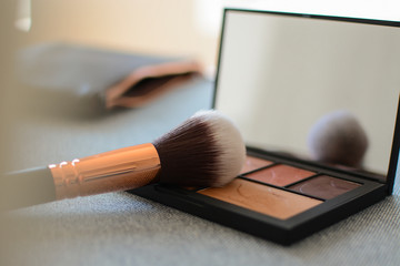 Make up palette close up in brown color tone and makeup brush tool on the sofa in the living room. 