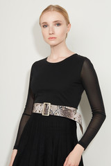 Cropped front view shot of a blond girl, wearing black dress with transparent sleeves and beige snake print wide belt with rectangular buckle and holes on it. Girl is posing on a white background. 
