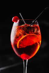 Wall Mural - An orange cocktail in a wine glass with an orange slice and a cherry. Aperol spritz. Dark background.