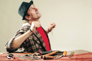 Wall Mural - Tired craftsman at workplace. Worker creates a new leather product in workshop. Crafting tools, leather on table. Handmade tools. Small business