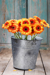 Fotomurales - Bouquet of orange gerbera daisies in silver bucket on wooden table.
