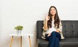 © Asier - Young arab woman sitting on the sofa winks an eye and holds an okay gesture with hand.