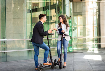 Wall Mural - Two business people with electric scooter talking outside in front of modern business building.