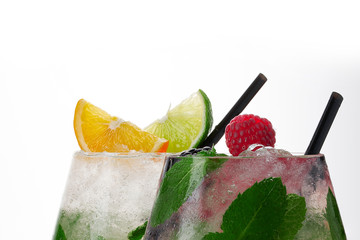 Two Glass of lemonade with lemon, lime,  raspberry and mint on white background. Colorful summer drinks with raspberry and orange and lime.