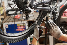 Cropped Shot Of Professional Mechanic Working In Bicycle Repair Shop, Serviceman Repairing Bike Chain Using Special Tool, Wearing Protective Workwear And Gloves