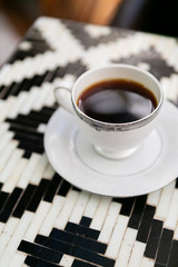 Cup of black coffee in vintage tea cup, black and white tile table, close up, modern cafe