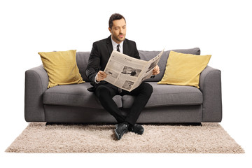 Wall Mural - Young businessman sitting on a sofa and reading a newspaper