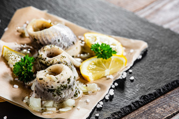 Marinated herring fillets on piece of paper on black stone