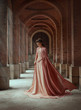 Sad princess in a vintage royal nude powdery color dress and in a cloak that flies in the wind. The magical Rays of the sun and hope pour on a woman through the columns. Long dark hair with a tiara.