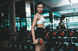 © Johnstocker - The woman stood holding a dumbbell at the thigh in the gym.