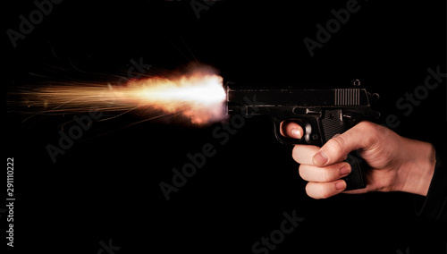 Gun in hand on black background. The threat of a firearm during a robbery on a dark street. Assault with a semiautomatic weapon. A shot from a pistol on a black background
