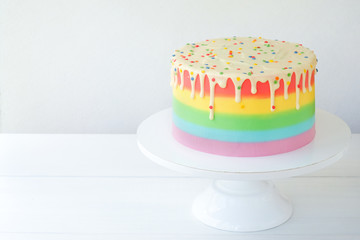 Wall Mural - Cake blank with colorful rainbow cream on a white background decorated with colorful sprinkles, poured with chocolate. Simple minimalism.