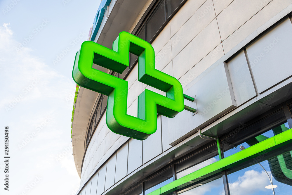 Close-up of green cross - sign of pharmacy on glass building - obrazy, fototapety, plakaty 